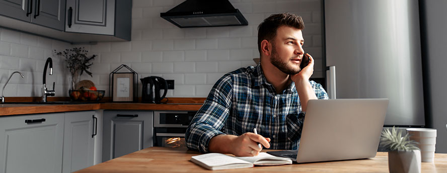 Male Person Wearing Shirt Working From Home In The Kitchen And Talking On The Phone