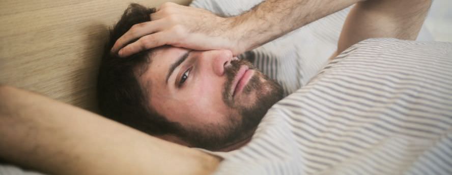 Man With Beard Lying On Bed With Headache Trying To Fall Asleep